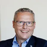 Franz Josef Schattleiter, Prokurist und Werksleiter der NÖM AG, sitzt an einem Schreibtisch und lächelt in die Kamera.