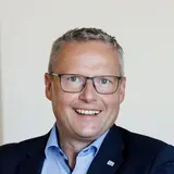 Franz Josef Schattleiter, Prokurist und Werksleiter der NÖM AG, sitzt an einem Schreibtisch und lächelt in die Kamera.