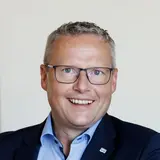 Franz Josef Schattleiter, Prokurist und Werksleiter der NÖM AG, sitzt an einem Schreibtisch und lächelt in die Kamera.