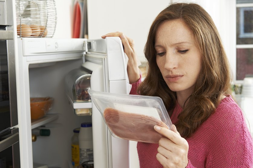 Eine Frau studiert vor ihrem Kühlschrank die Lebensmittelkennzeichnung auf einer Verpackung.