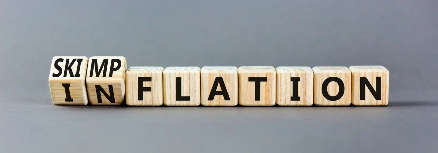 Der Begriff „Skimpflation“ auf Holzwürfeln: Das Wort beschreibt die Veränderung von Lebensmittelrezepturen.