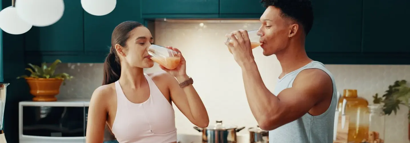 Paar in Sportkleidung steht in der Küche und trinkt einen Protein-Drink.
