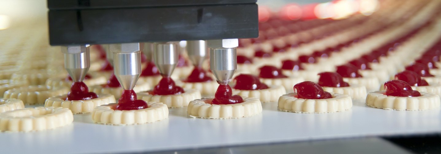Eine moderne Produktionsmaschine gibt Marmelade auf industriell hergestellte Kekse.