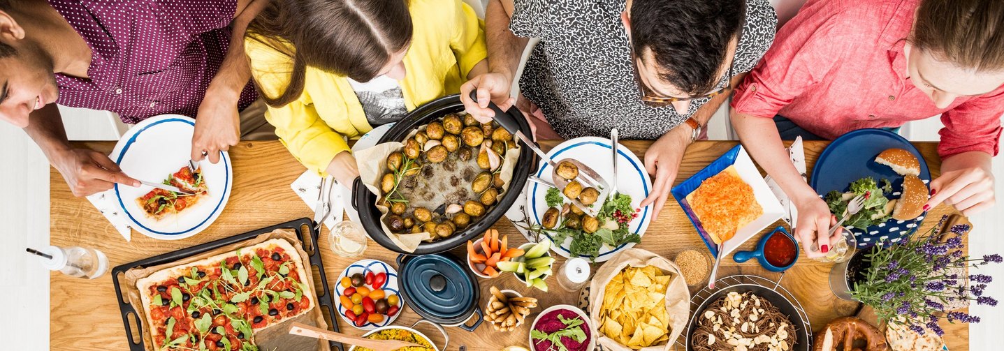 Vegetarische Speisen auf Tisch: Bratkartoffeln, Pizza, Hummus und Bulgur.