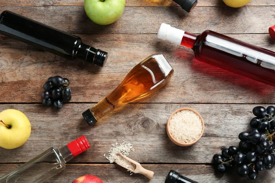 Verschiedene Essigsorten wie Balsamico, Apfelessig oder Weinessig liegen flach auf einem Holztisch.