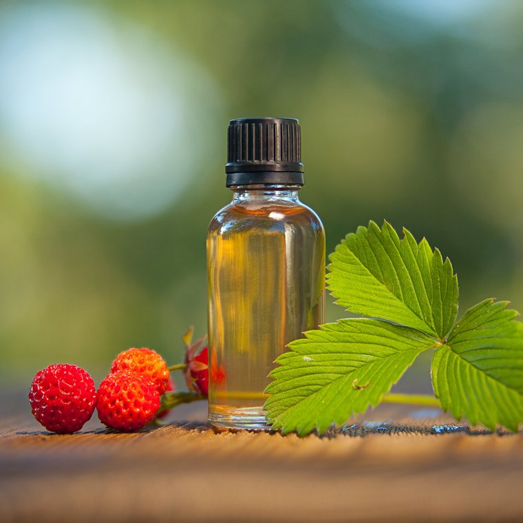 Erdbeeraroma in einem Glasfläschchen auf einem Holztisch, daneben wilde Erdbeeren und Blätter