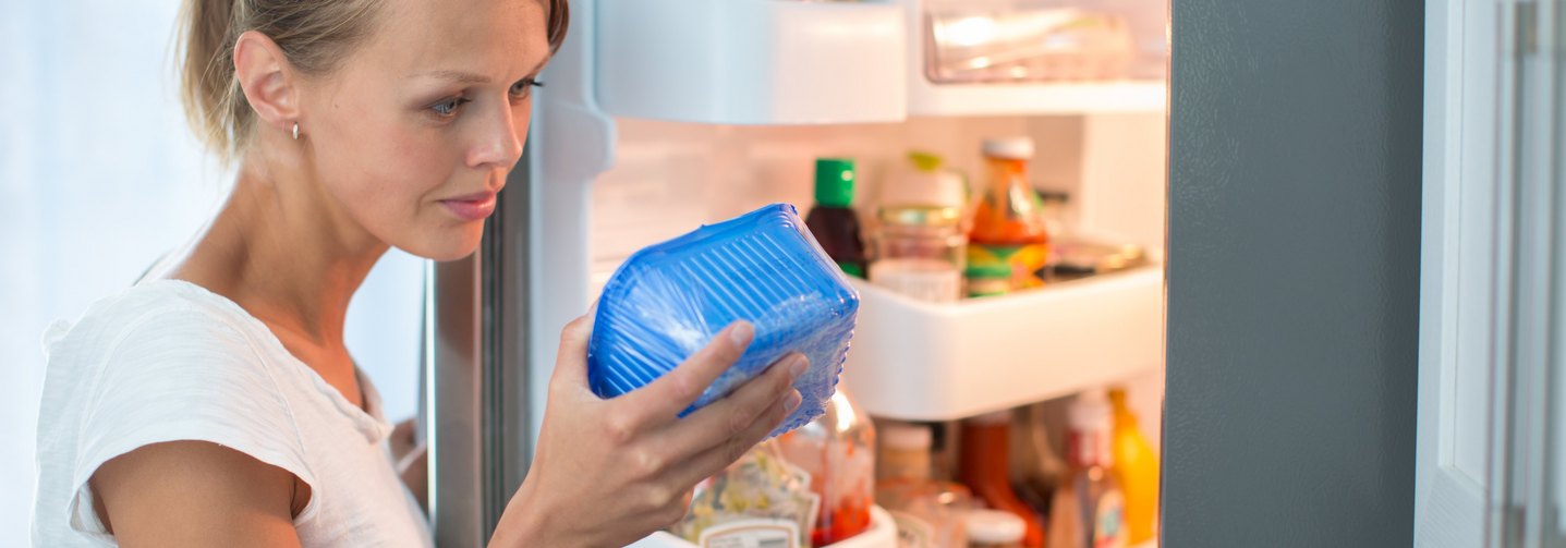 Eine Konsumentin betrachtet ein verpacktes Lebensmittel, das sie aus dem Kühlschrank geholt hat.