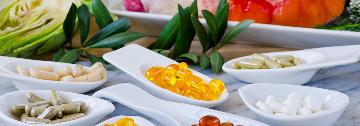 Diverse Nahrungsergänzungsmittel auf verschiedene Schüsseln aufgeteilt, dahinter unter anderem Lachs und Knoblauch.