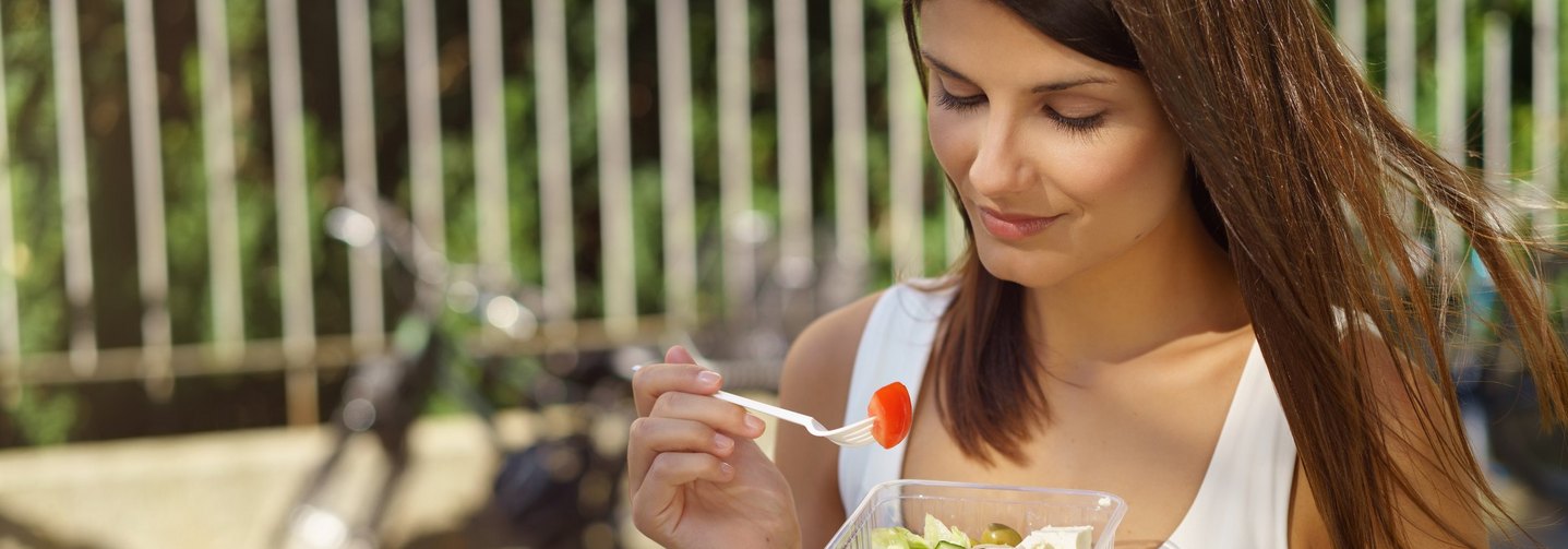 Junge Frau ist in der Stadt unterwegs und isst einen Salat.