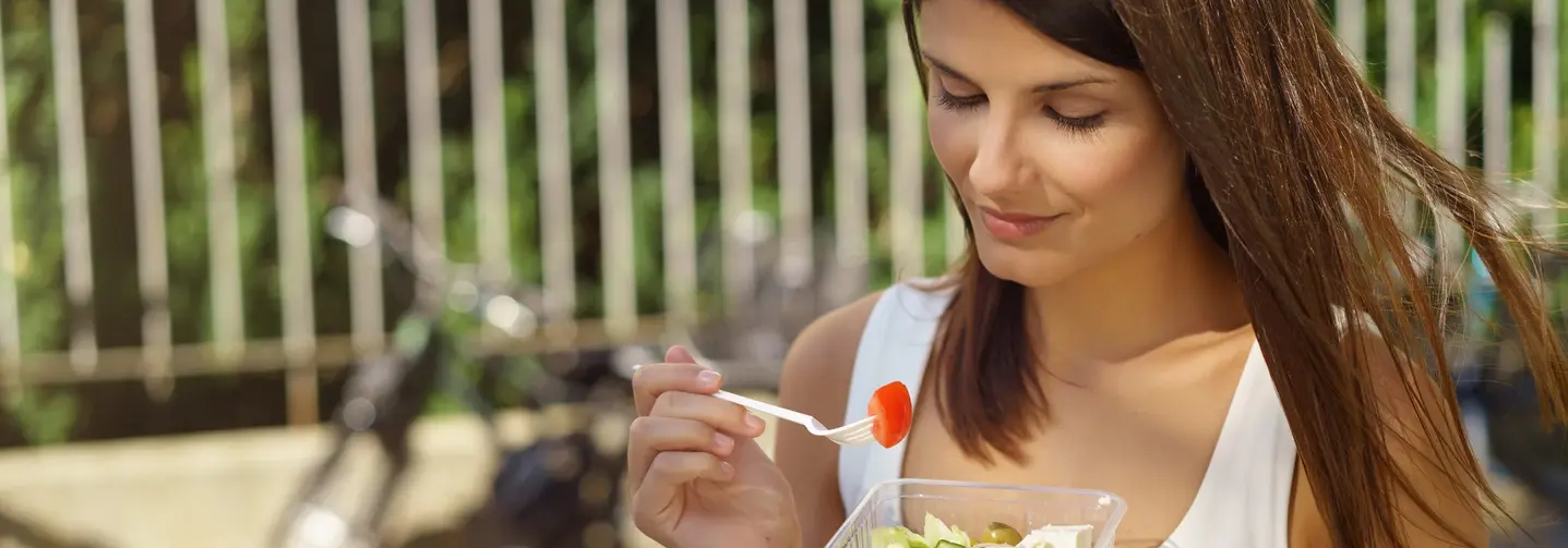 Junge Frau ist in der Stadt unterwegs und isst einen Salat.