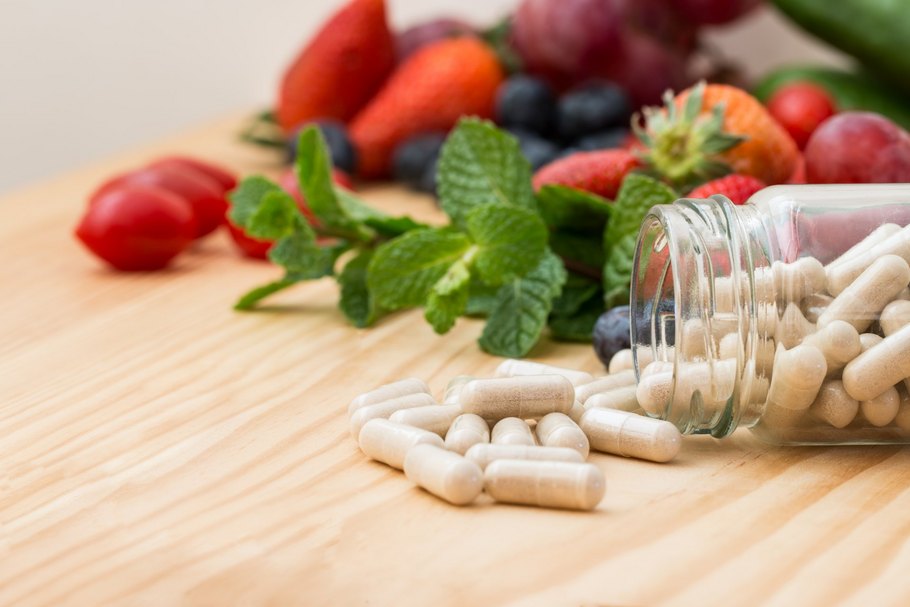 Vitaminpillen auf einem Tisch vor Obst: Nahrungsergänzungsmittel werden auch eingesetzt, um Nährstoffdefizite bei einseitiger Ernährung auszugleichen.