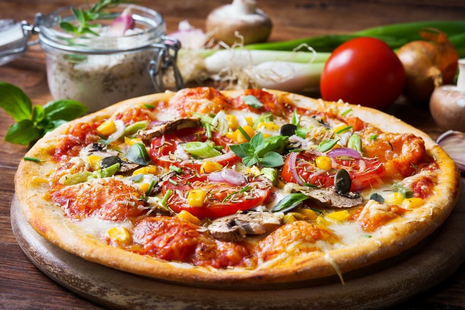 Vegetarische Pizza mit Gemüse und Kräutern liegt auf einem Tisch.