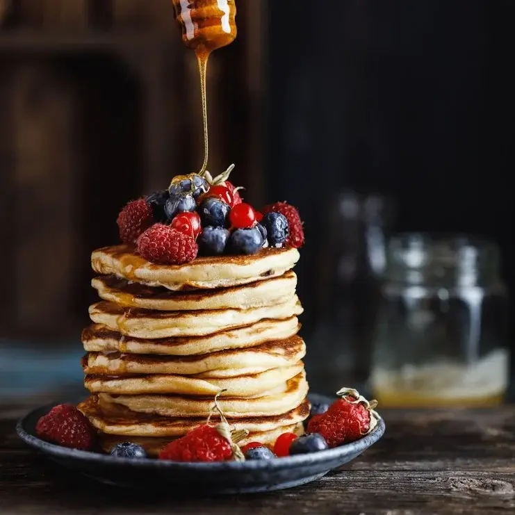 Nahaufnahme von Pfannkuchen mit Heidelbeeren und Himbeeren garniert auf einem Holztisch. 