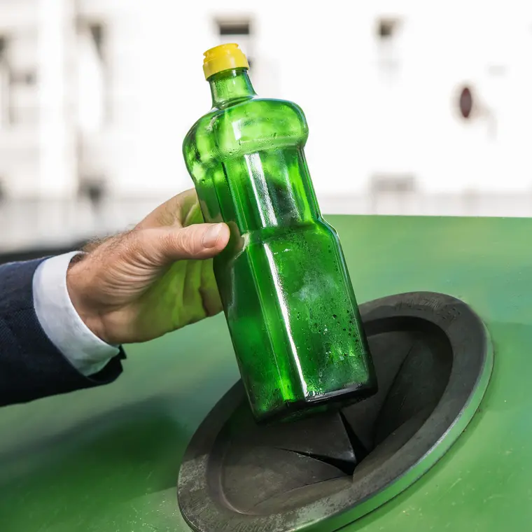Männerhand mit Buntstoffglasflasche beim Einwurf in einen Sammelbehälter