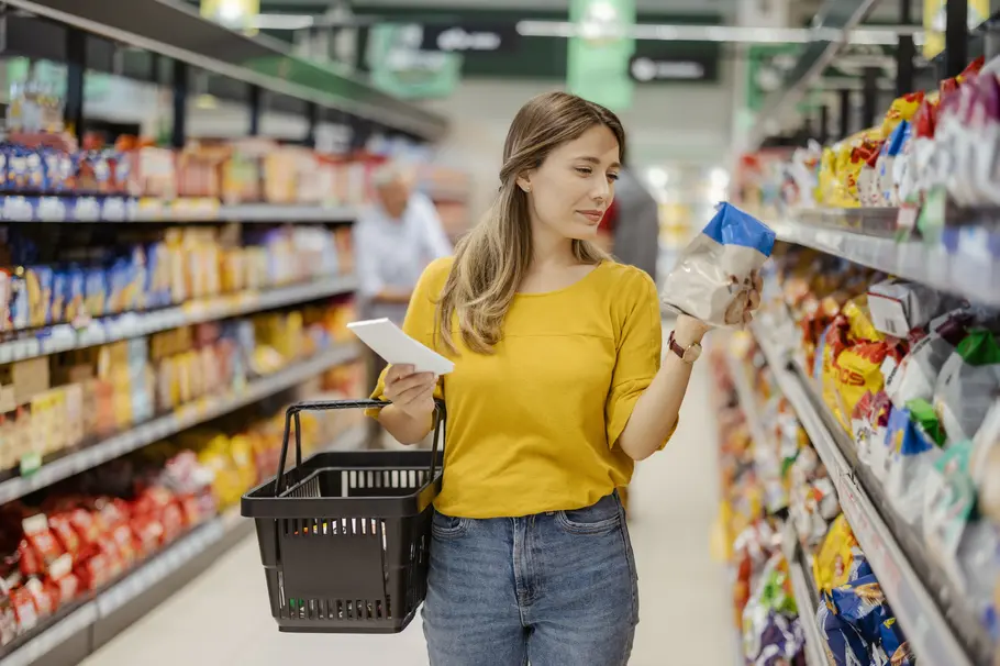 Eine Frau im Supermarkt prüft die Zutatenliste auf der Verpackung eines Lebensmittels.