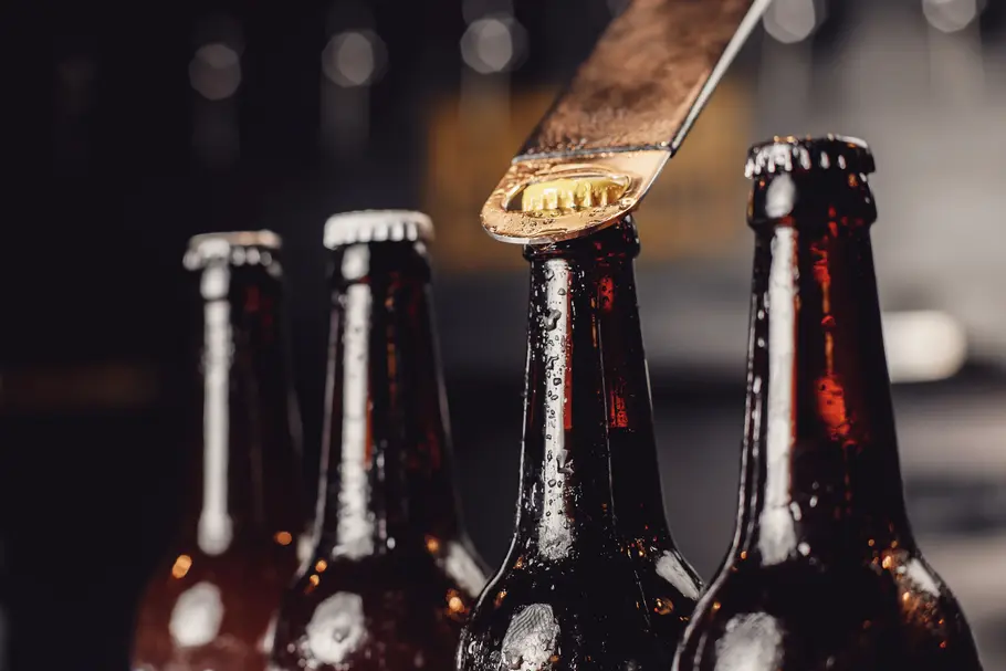 Vier braune Bierflaschen mit goldfarbenen und silbernen Metallverschlüssen und Flaschenöffner.