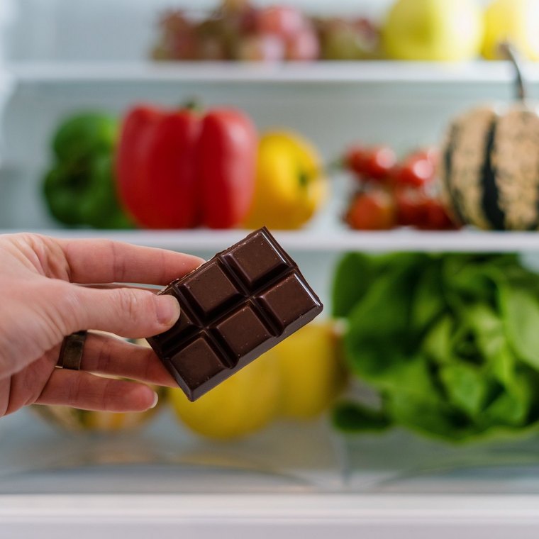 Schokolade vor einem gefüllten Kühlschrank: Dass das Kakaoerzeugnis im Kühlschrank gelagert werden sollte, stimmt nicht.