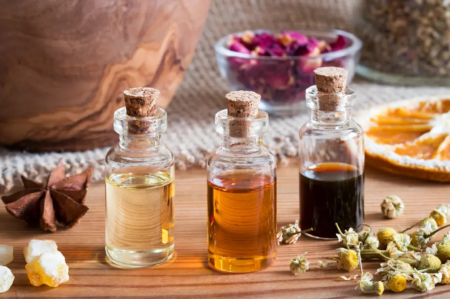 Drei kleine Glasfläschchen gefüllt mit verschiedenen natürlichen Aromen. Umgeben von Ausgangsstoffen wie Orangen, Rosenblättern, Kamille und Sternanis.
