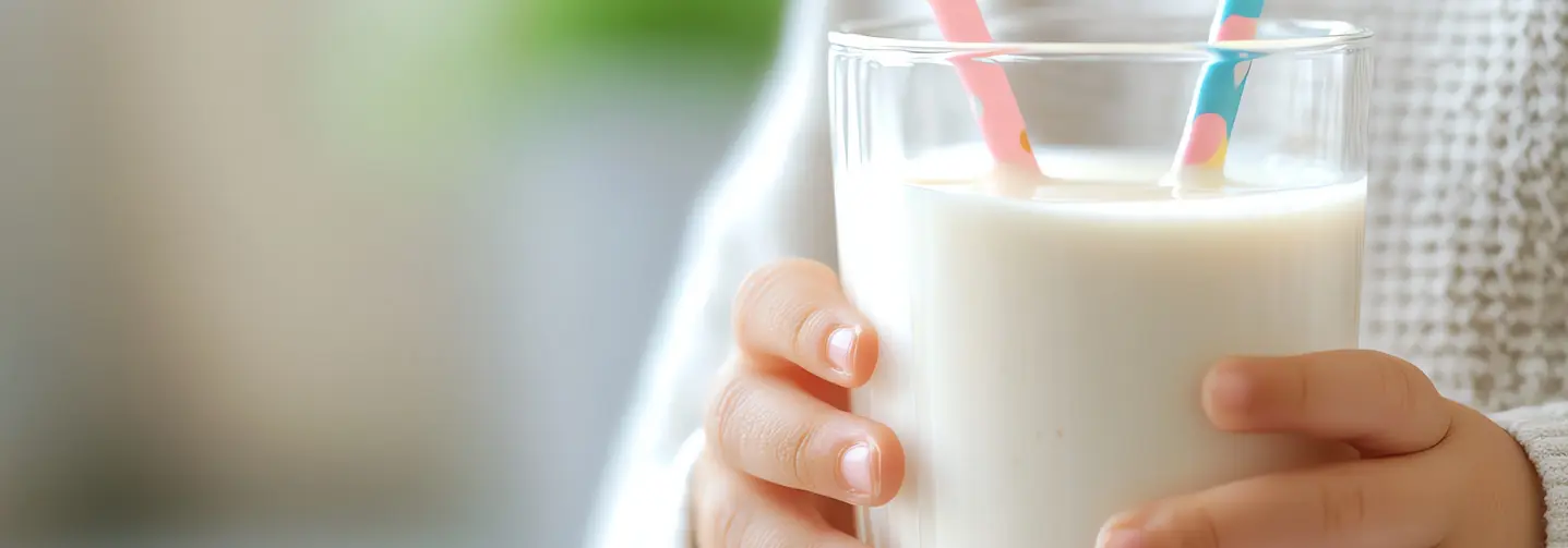 Kinderhände halten ein großes Glas gefüllt mit Milch, darin zwei bunte Strohhalme.