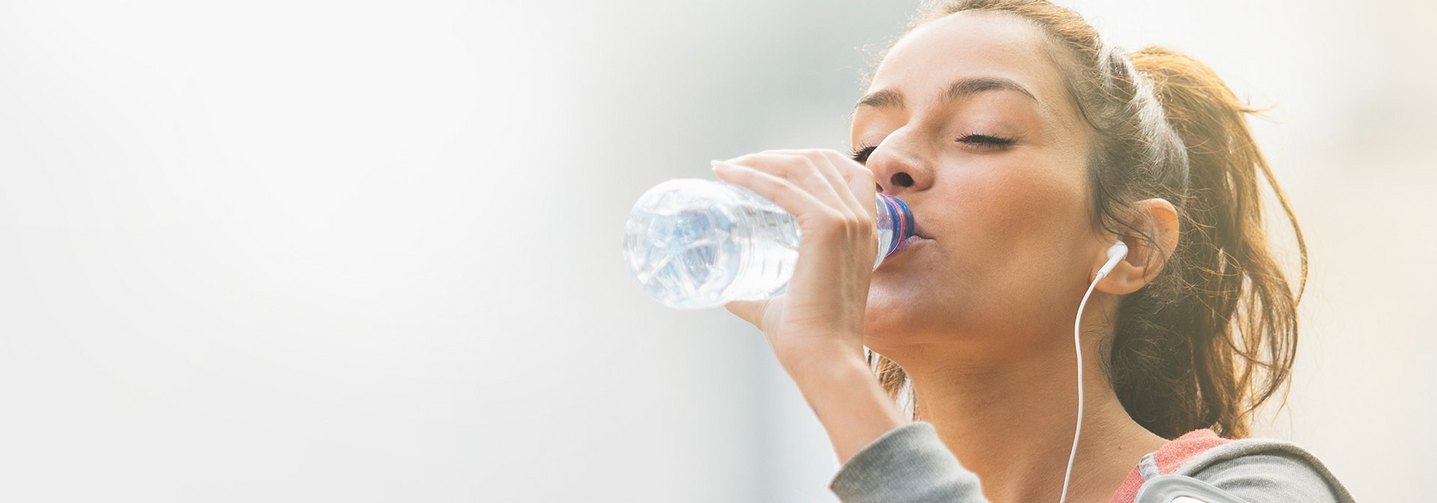 Junge Frau trinkt natürliches Mineralwasser aus einer Flasche.